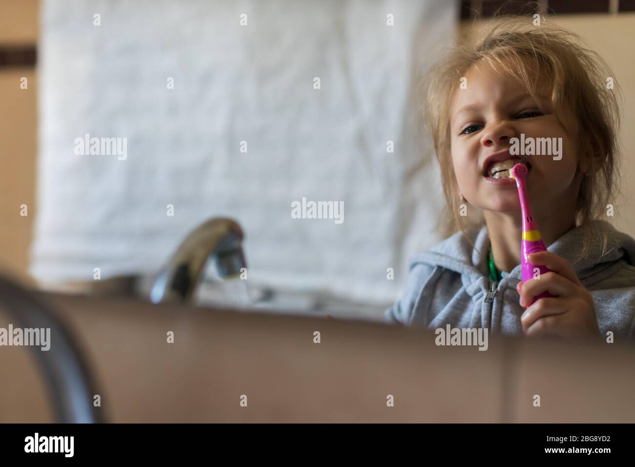 Emotional close up of a cute little girl brushing teeth with electric toothbrush. Stock Photo