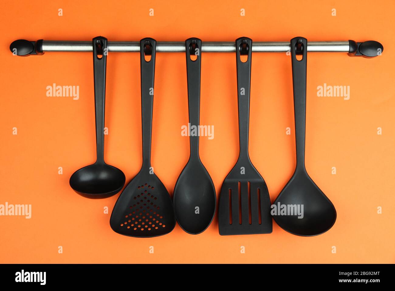 Plastic kitchen utensils on silver hooks on orange background Stock Photo