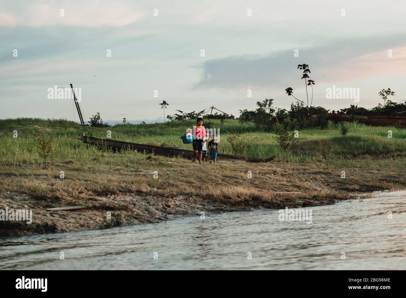 Mother holding laundry stands by her sons on Amazon River bank at dusk  - jungle life near Iquitos, Peru Stock Photo