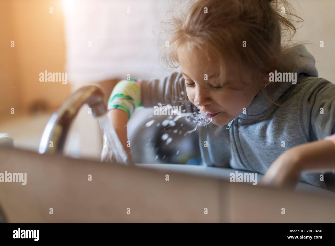 Cute little child girl rinses her mouth with water, looking at mirror and spits water into the sink Stock Photo