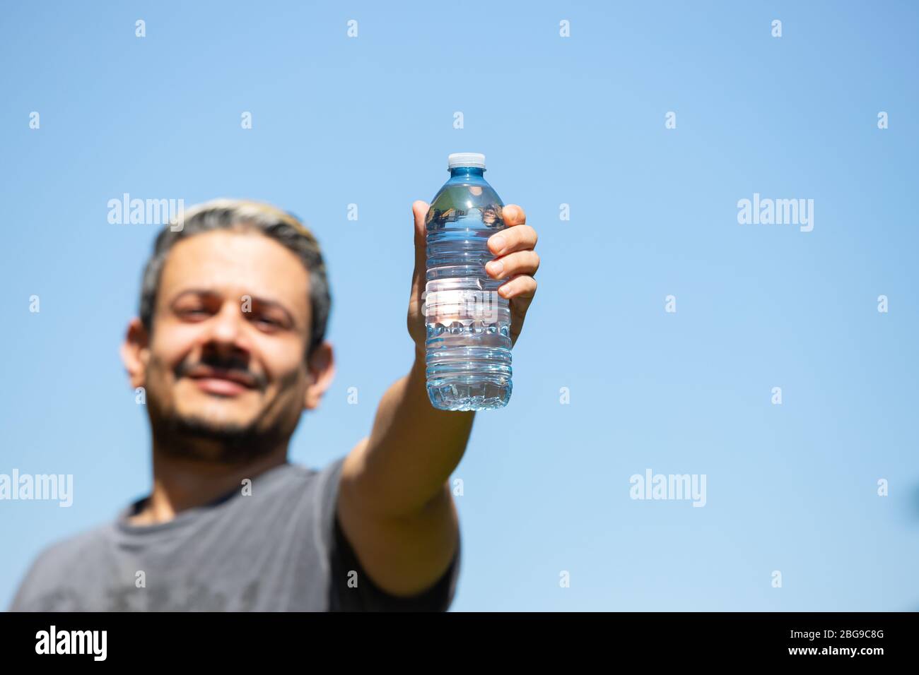 https://c8.alamy.com/comp/2BG9C8G/happy-man-holding-up-a-clear-water-bottle-against-a-blue-sky-background-2BG9C8G.jpg