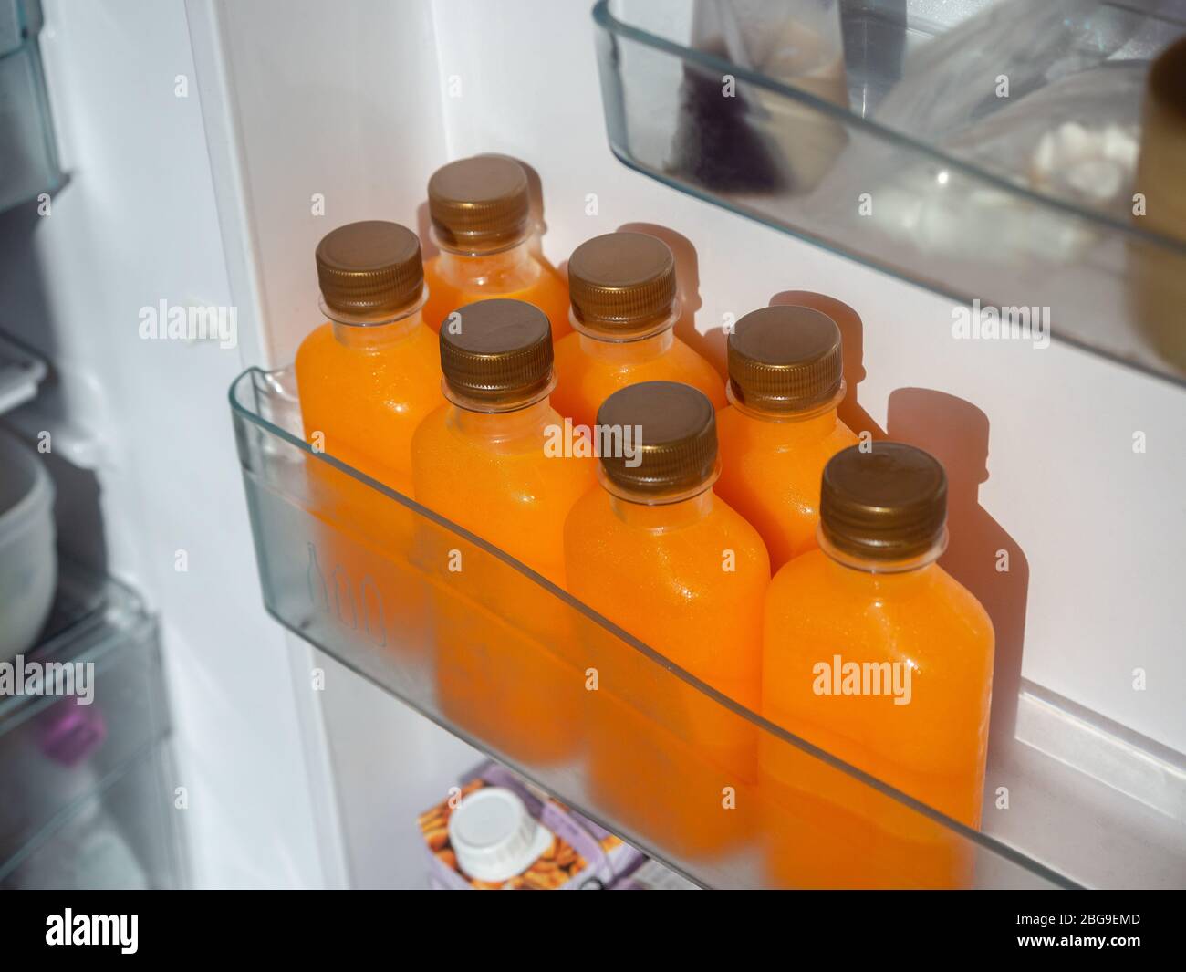 Orange juice iced cold in the bottles on shelf in refrigerator. Square shape bottle with cold orange juice, top view. Stock Photo