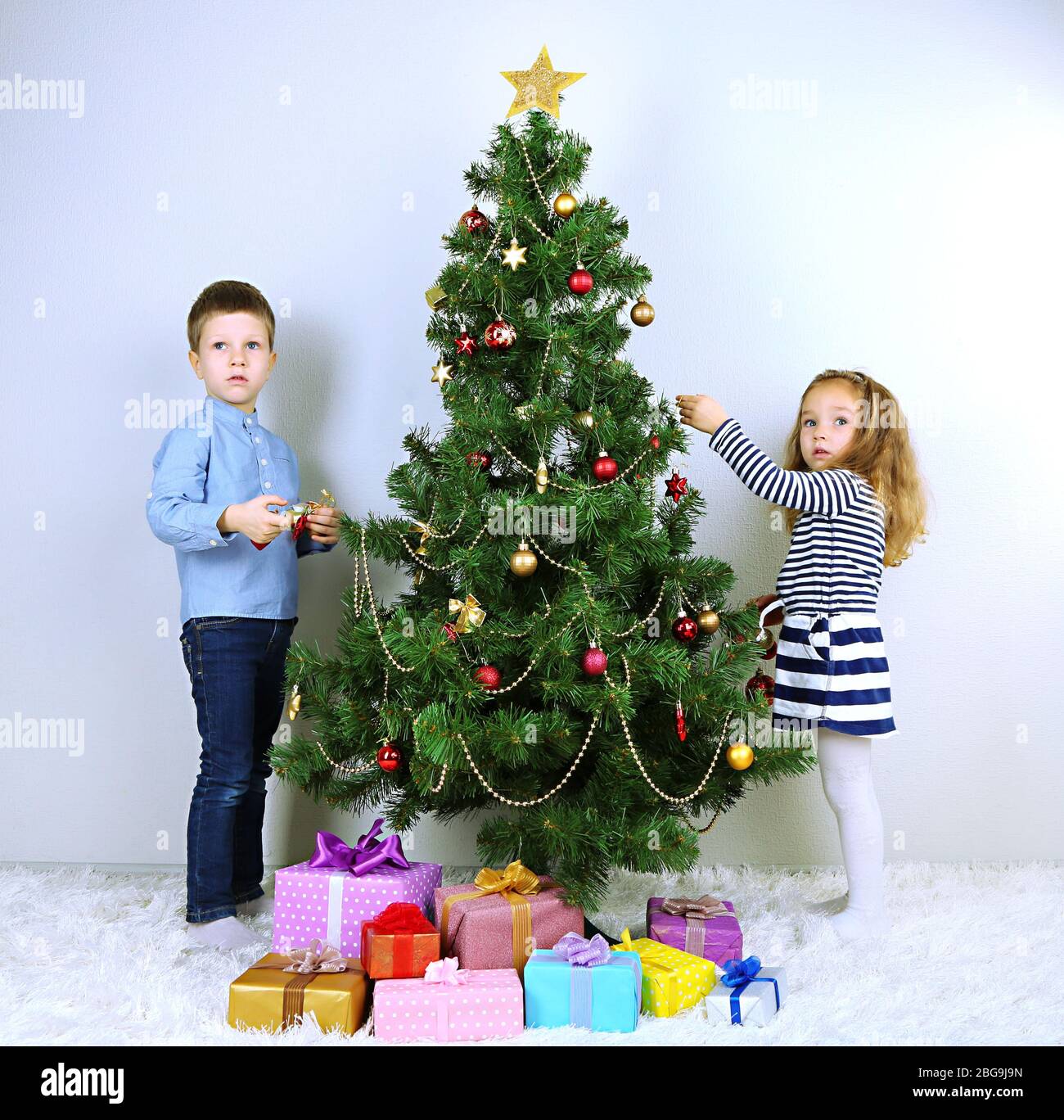 Kids decorating Christmas tree with baubles in room Stock Photo Alamy