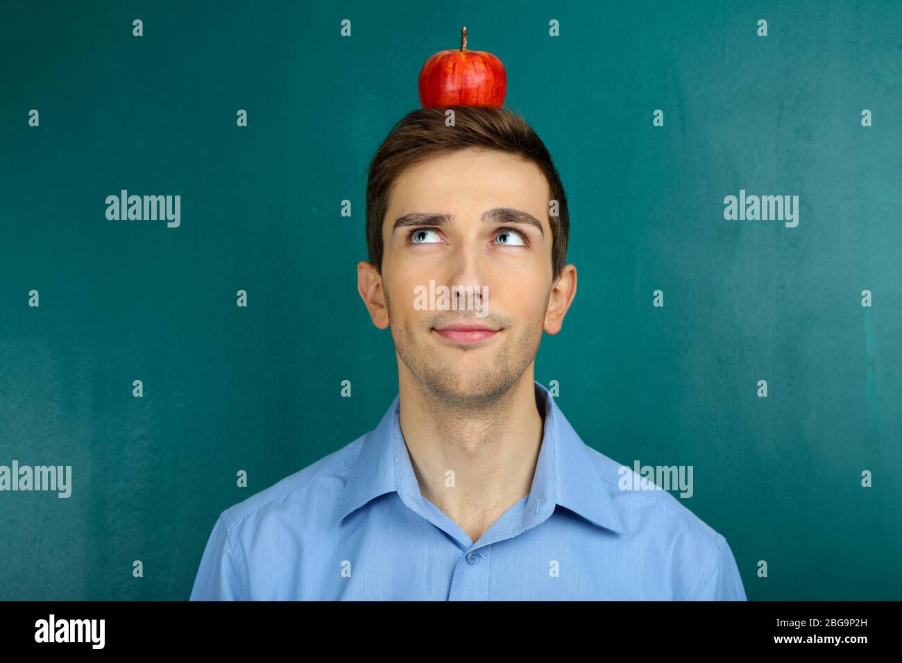 Young teacher with apple on his heard on chalkboard background Stock Photo