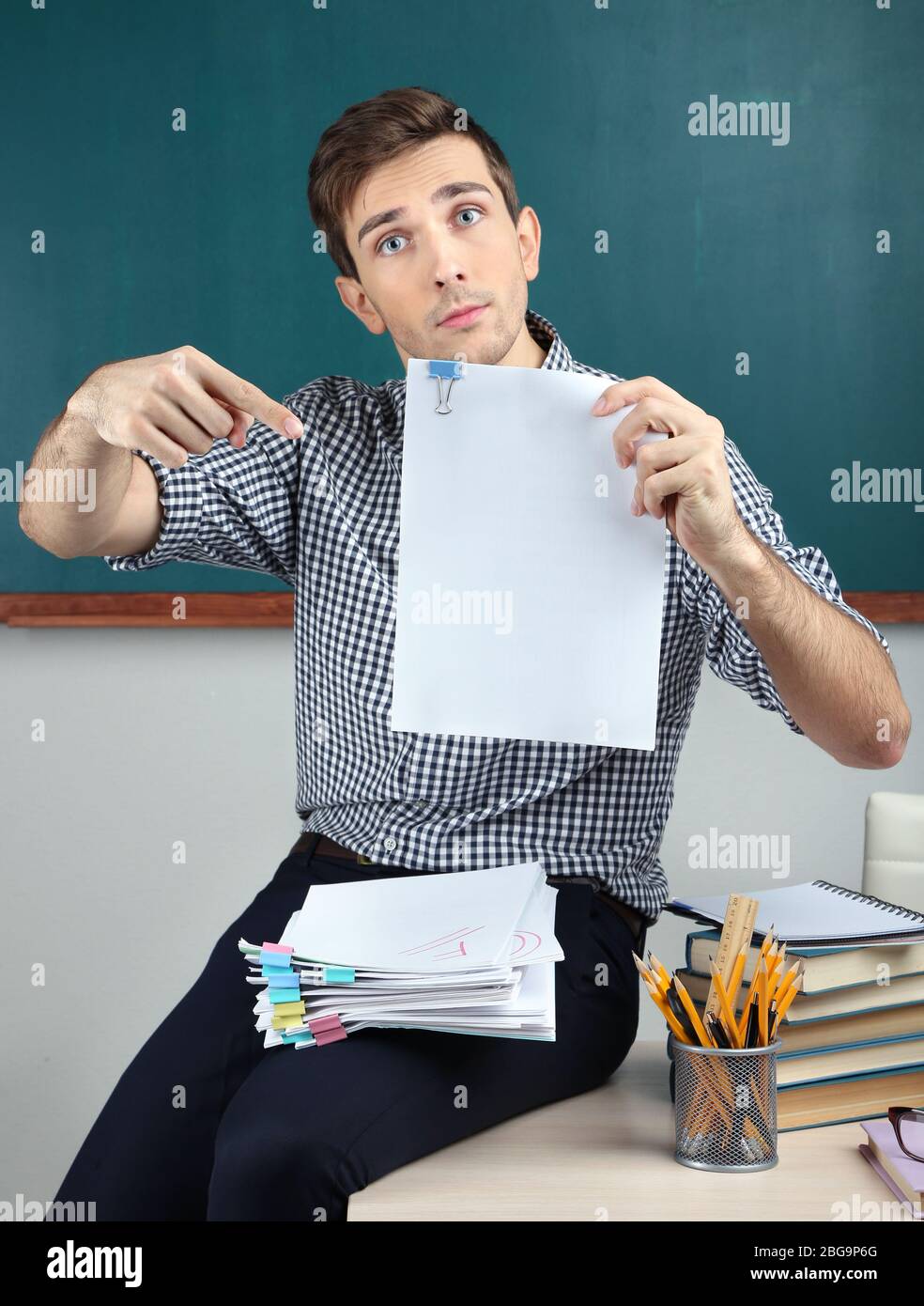 Young teacher sitting on desk in school classroom Stock Photo - Alamy