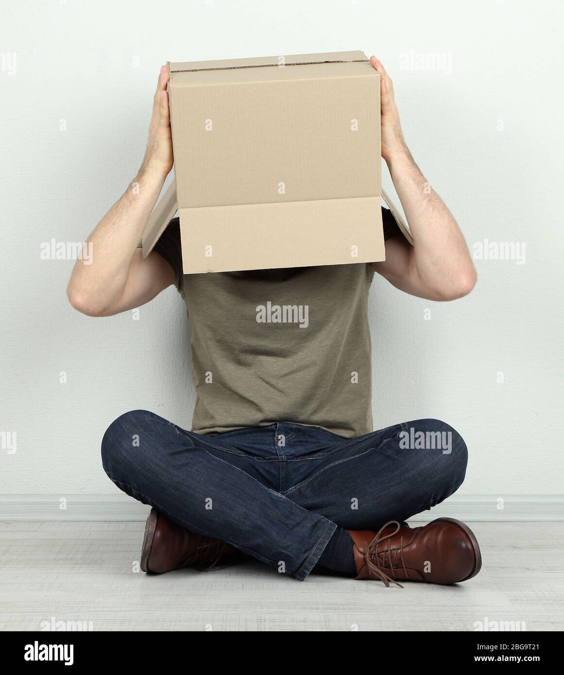 Man with cardboard box on his head sitting on floor near wall Stock ...