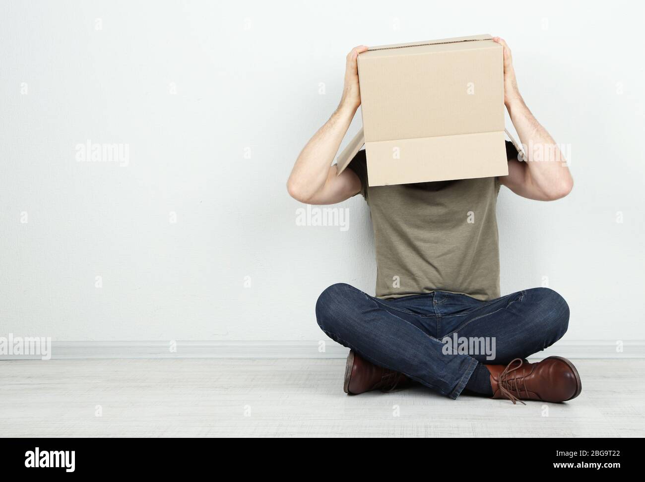 Man with cardboard box on his head sitting on floor near wall Stock ...