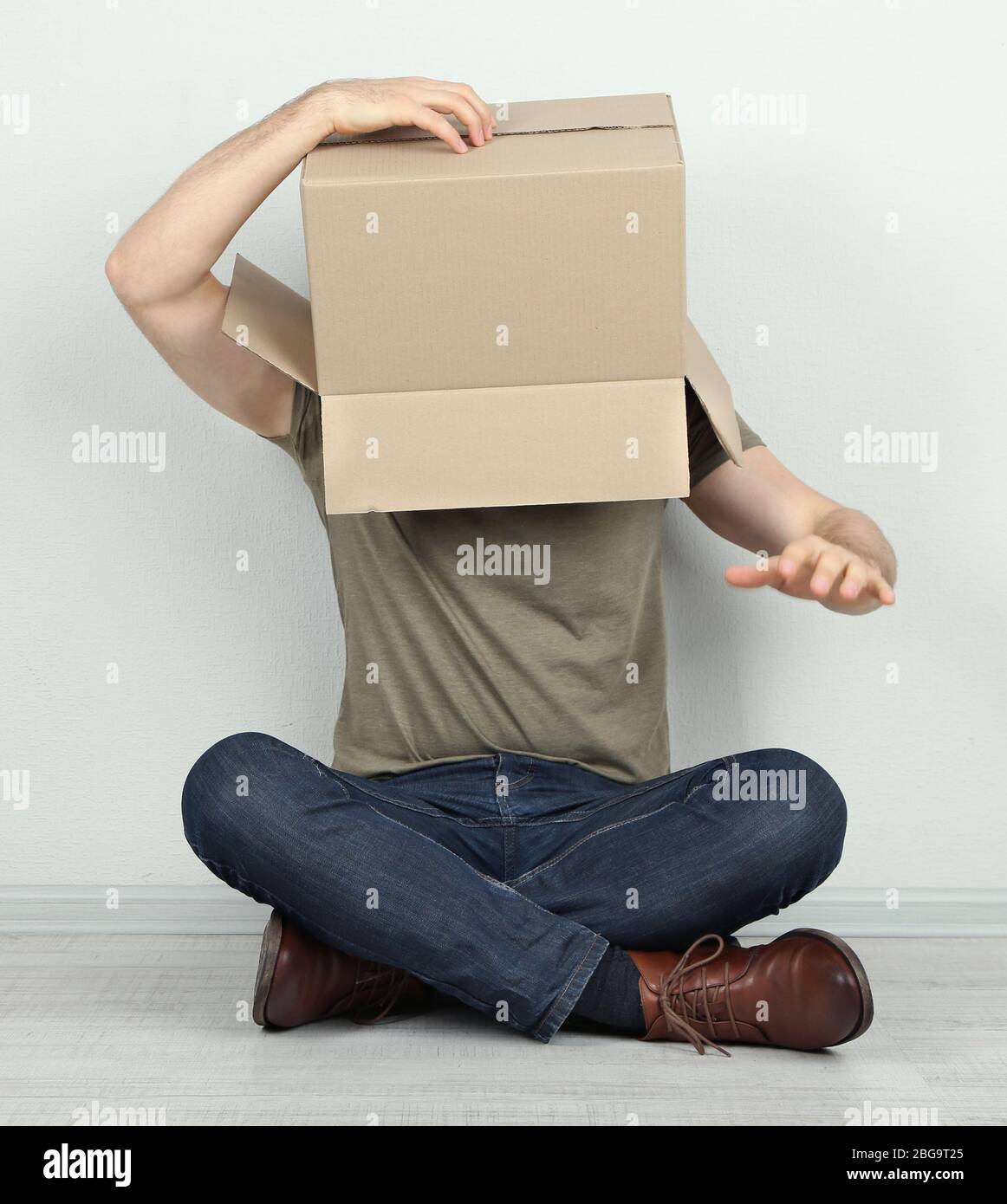 Man with cardboard box on his head sitting on floor near wall Stock ...
