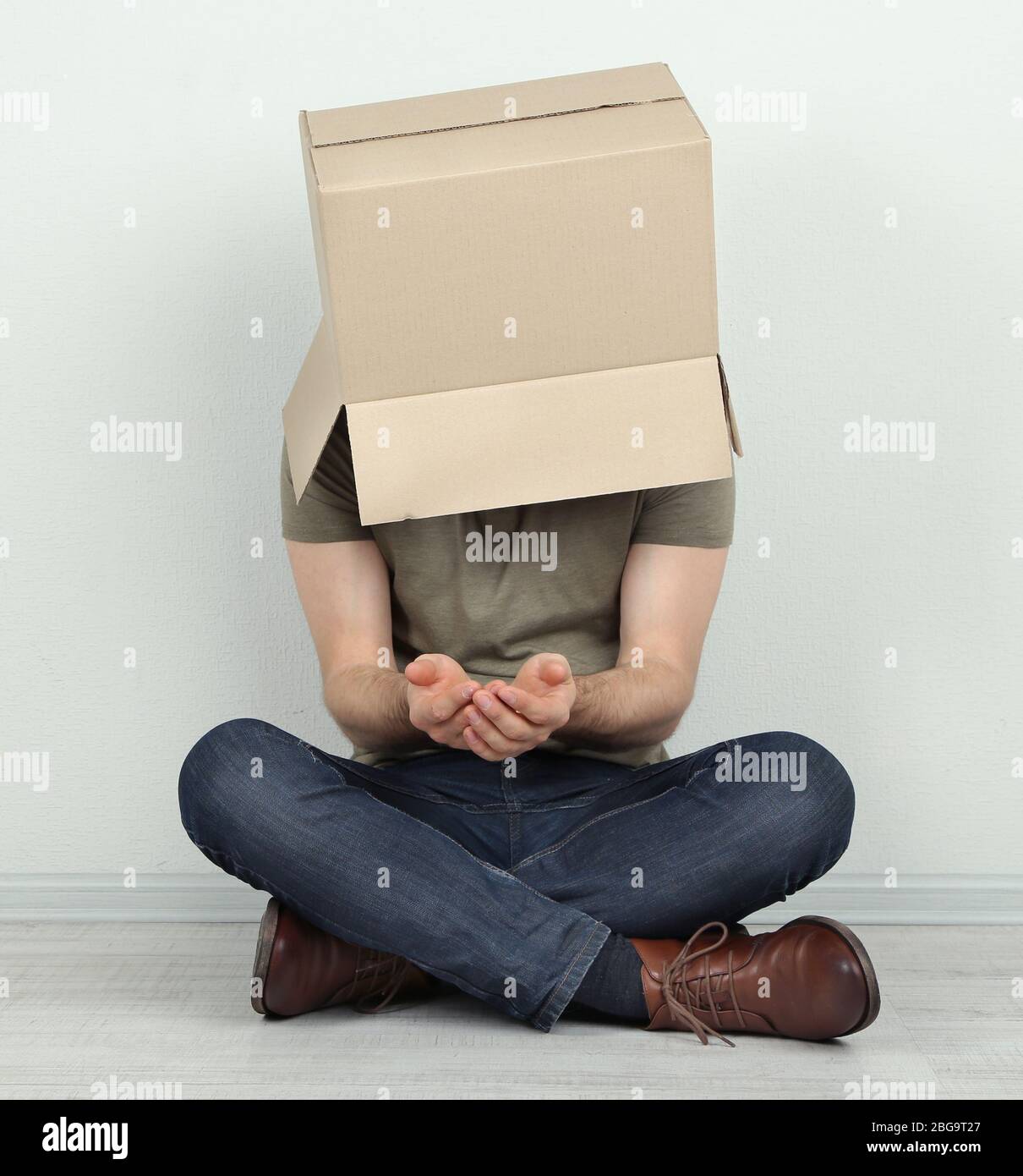Man with cardboard box on his head sitting on floor near wall Stock ...