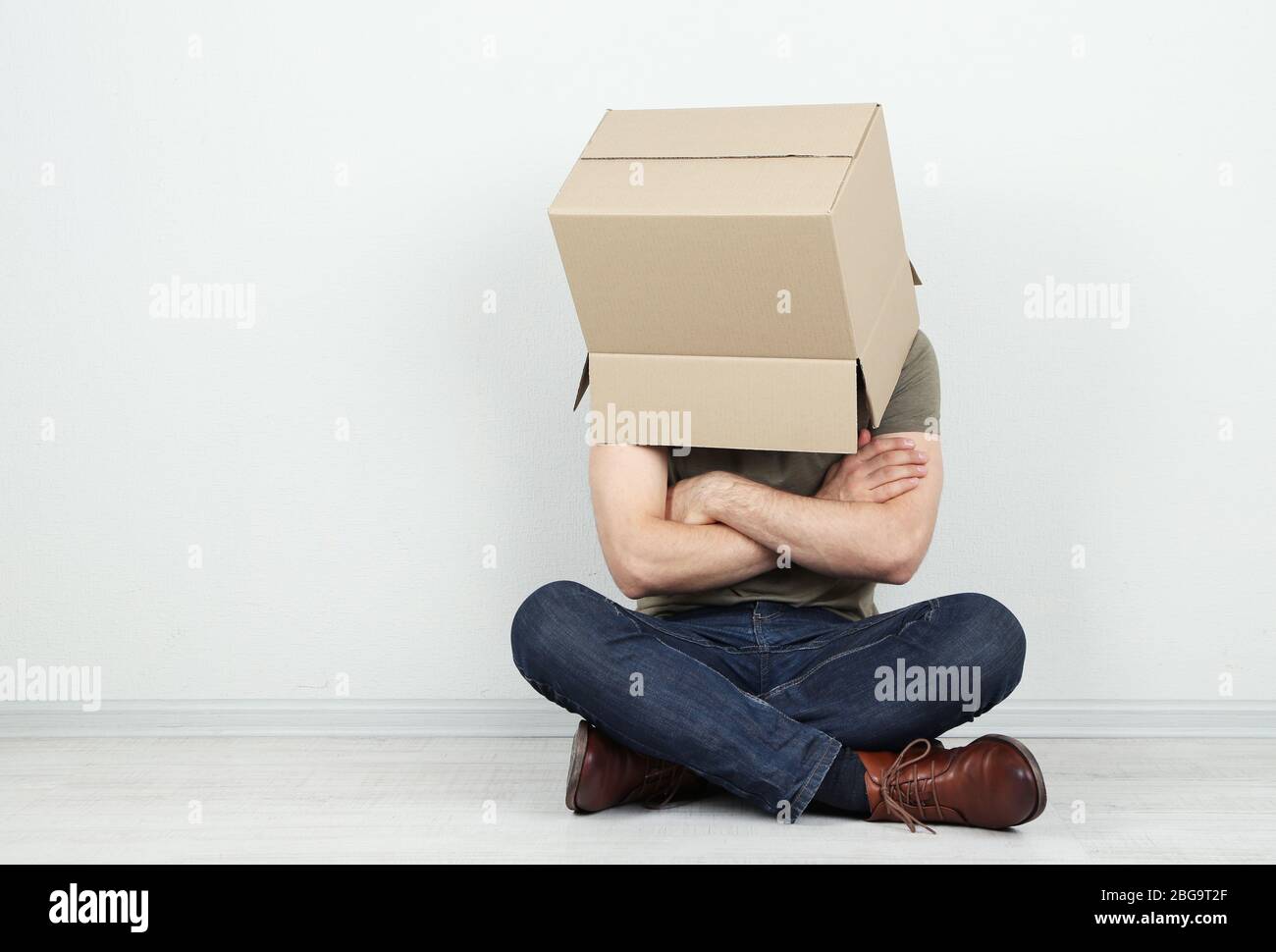 Man with cardboard box on his head sitting on floor near wall Stock ...