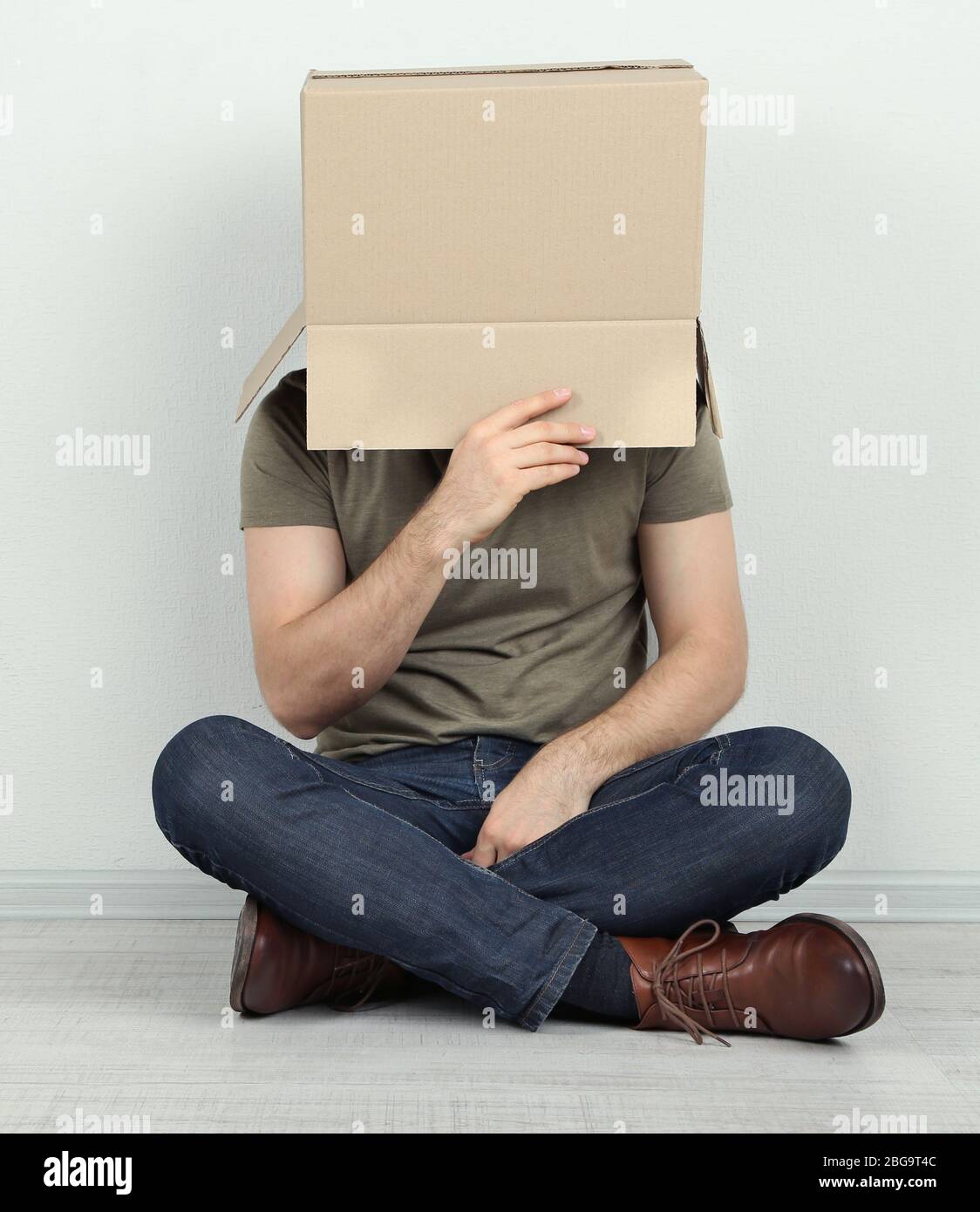 Man with cardboard box on his head sitting on floor near wall Stock ...