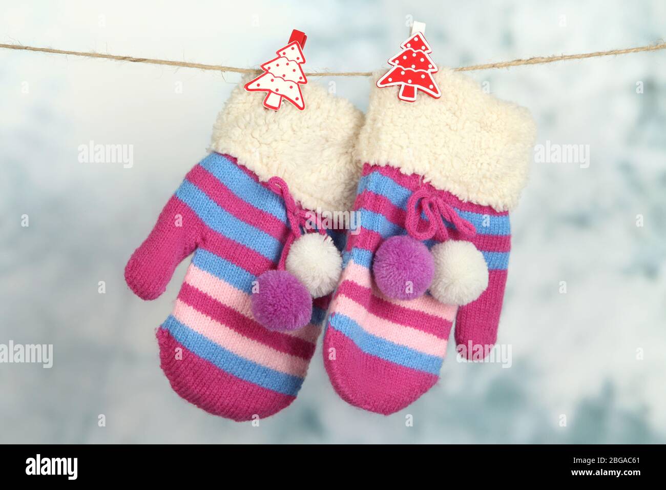 Striped mittens hanging on clothesline on bright background Stock Photo