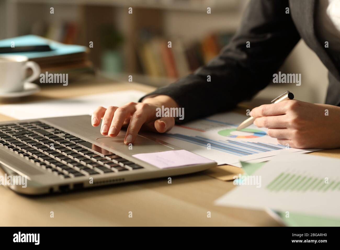 Close up of entrepreneur woman hands comparing graph report on laptop at night Stock Photo
