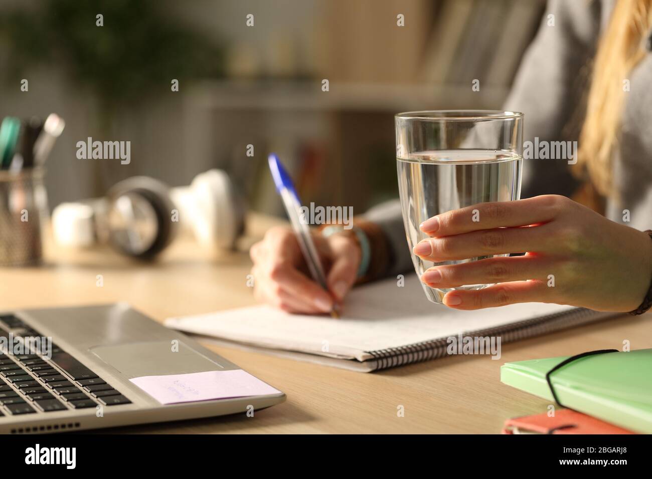 Close up of student girl hands holding glass of water at night studying siting on a desk Stock Photo