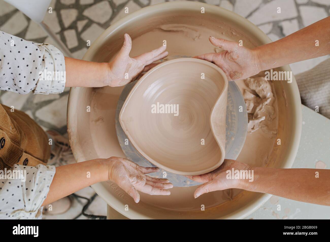 Two sets of hands giving heart shape to a clay bowl. top view Stock Photo