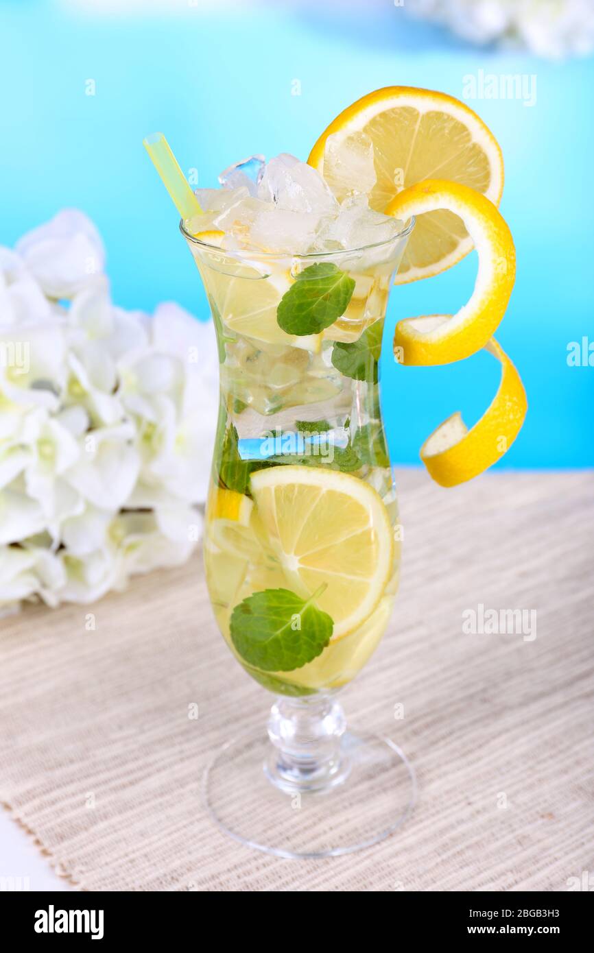 Glass of cocktail with lemon and mint on table on light blue background ...