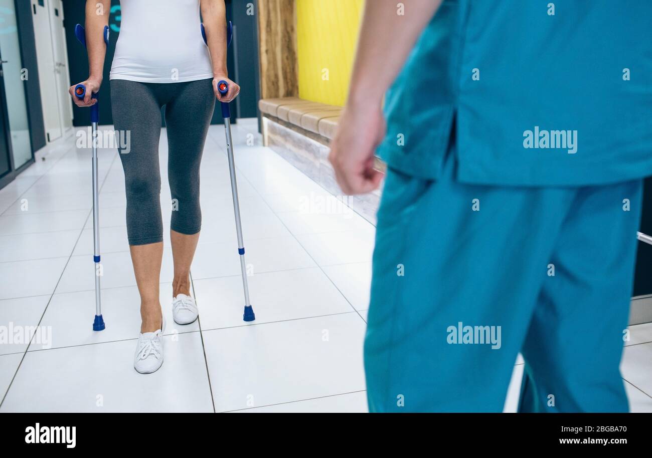 Woman patient using crutches for rehabilitation after injury. Physiotherapist assisting a patient. Stock Photo