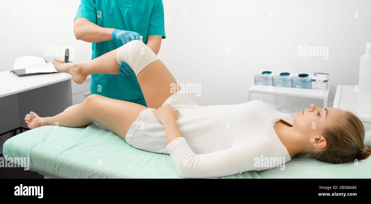 Traumatologist bandaging a woman's injured leg with an elastic bandage. Young woman injured her knee while doing sports Stock Photo