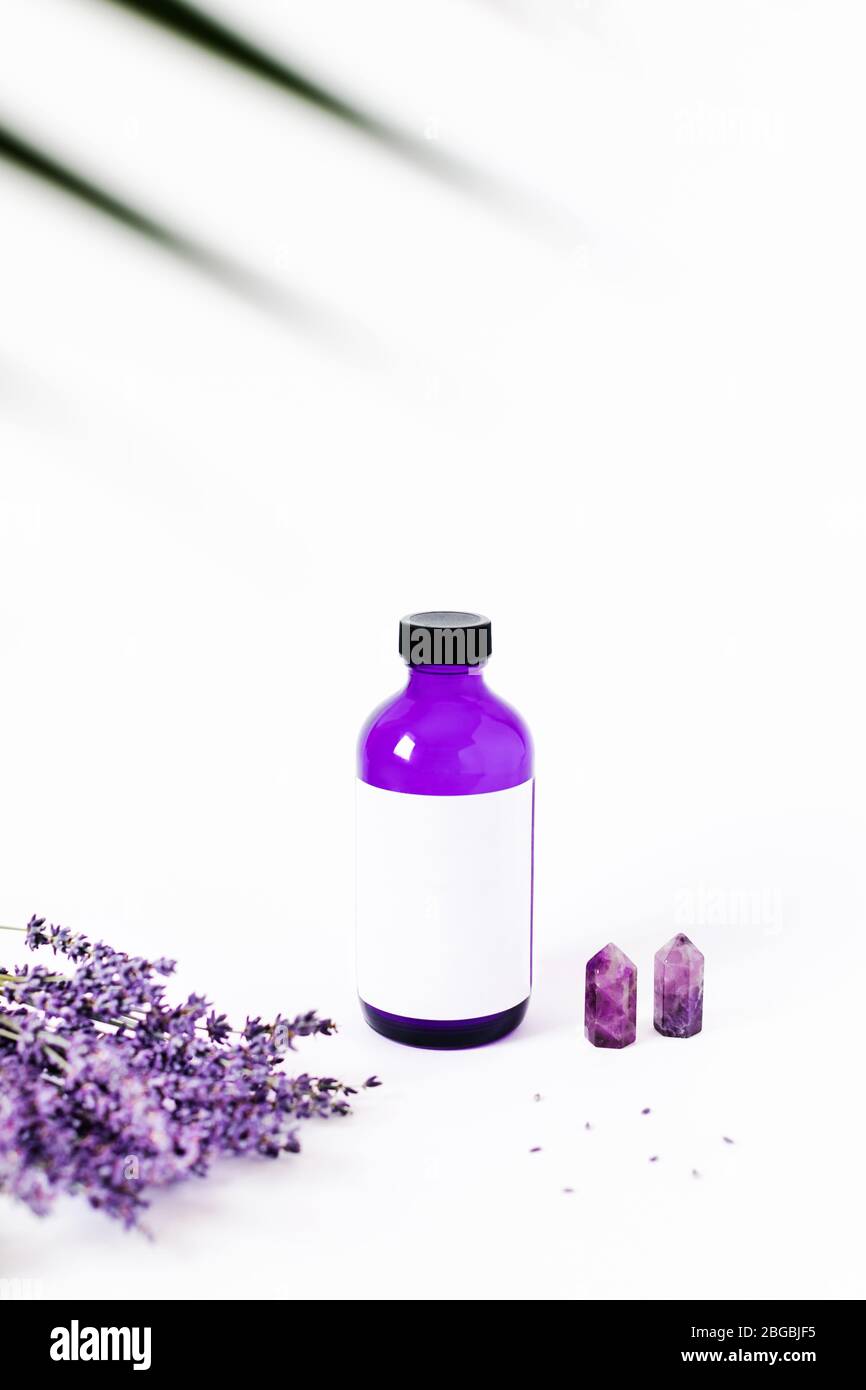 Glass bottle with body lotion, aroma oil on white background surrounded by lavender and the crystal of quartz. Stock Photo