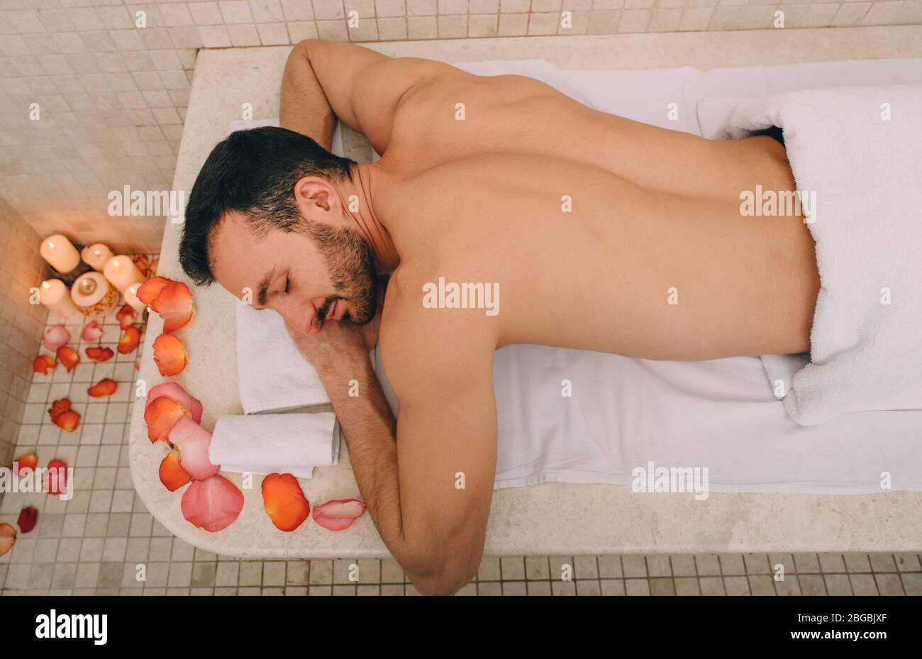 Caucasian man in romantic setting enjoys relaxing in Turkish bath. Hot marble table warms a man's body in a hammam Stock Photo