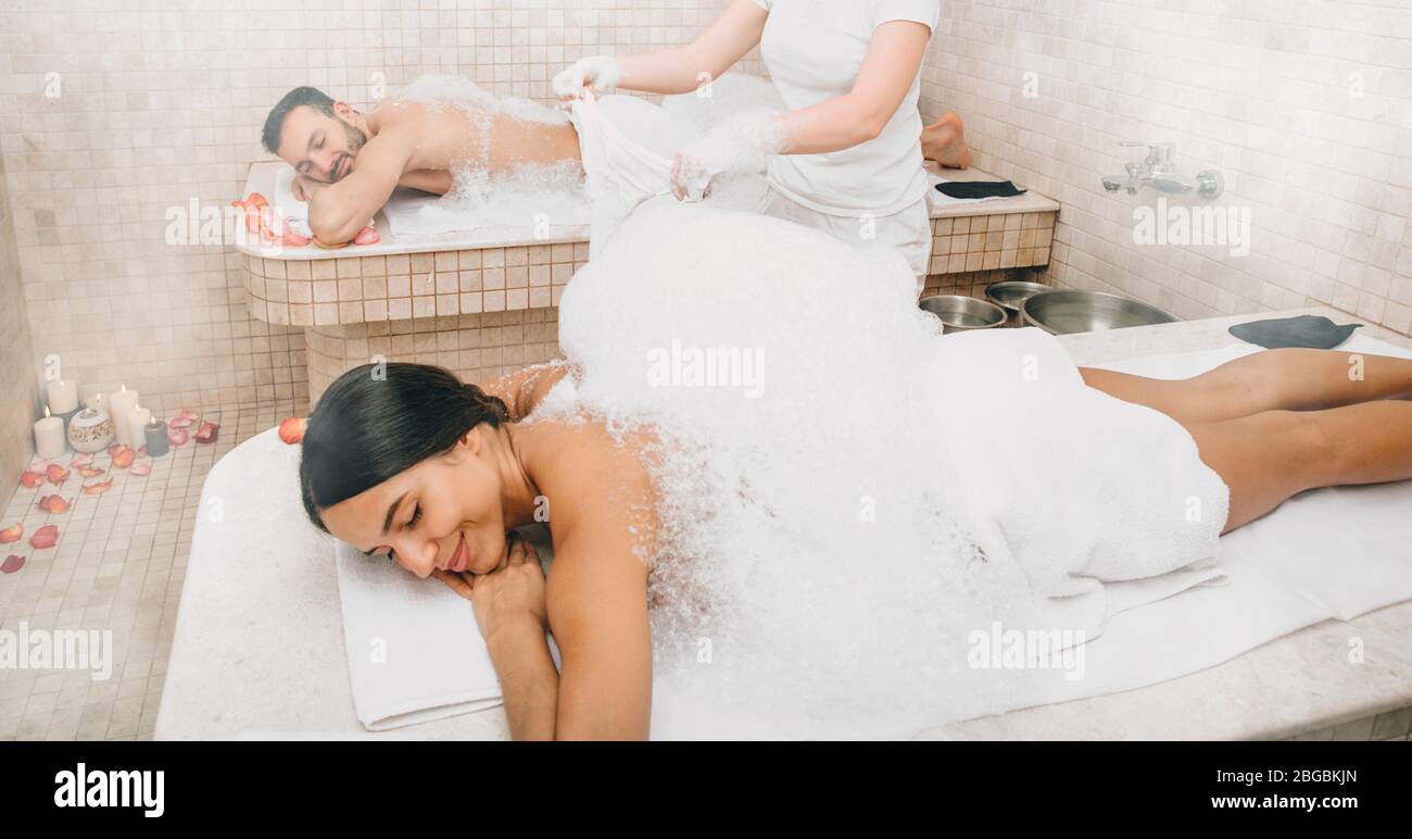 Mixed race couple is having fun and relaxing in a Turkish bath during a foam massage procedure. Hammam workers wash their bodies with soap and foam Stock Photo