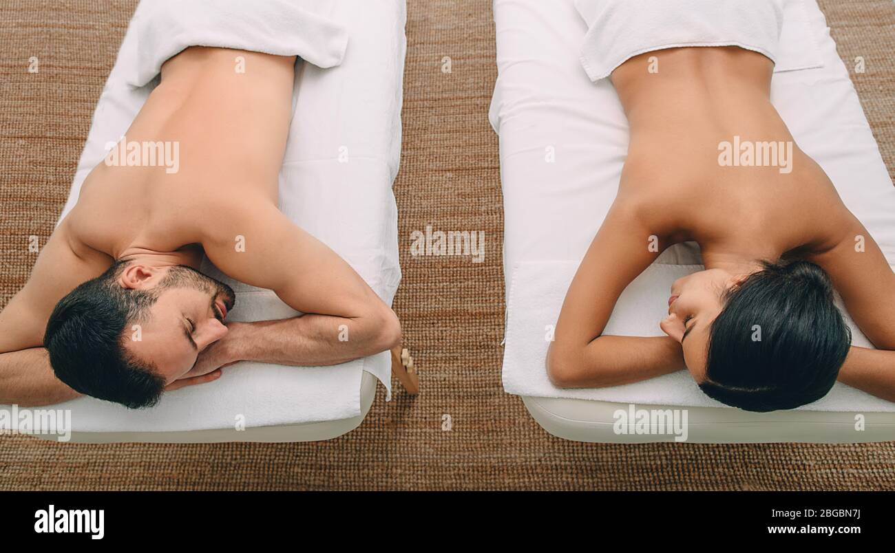 Beautiful mixed race couple enjoying relaxation at the spa while lying on massage tables Stock Photo