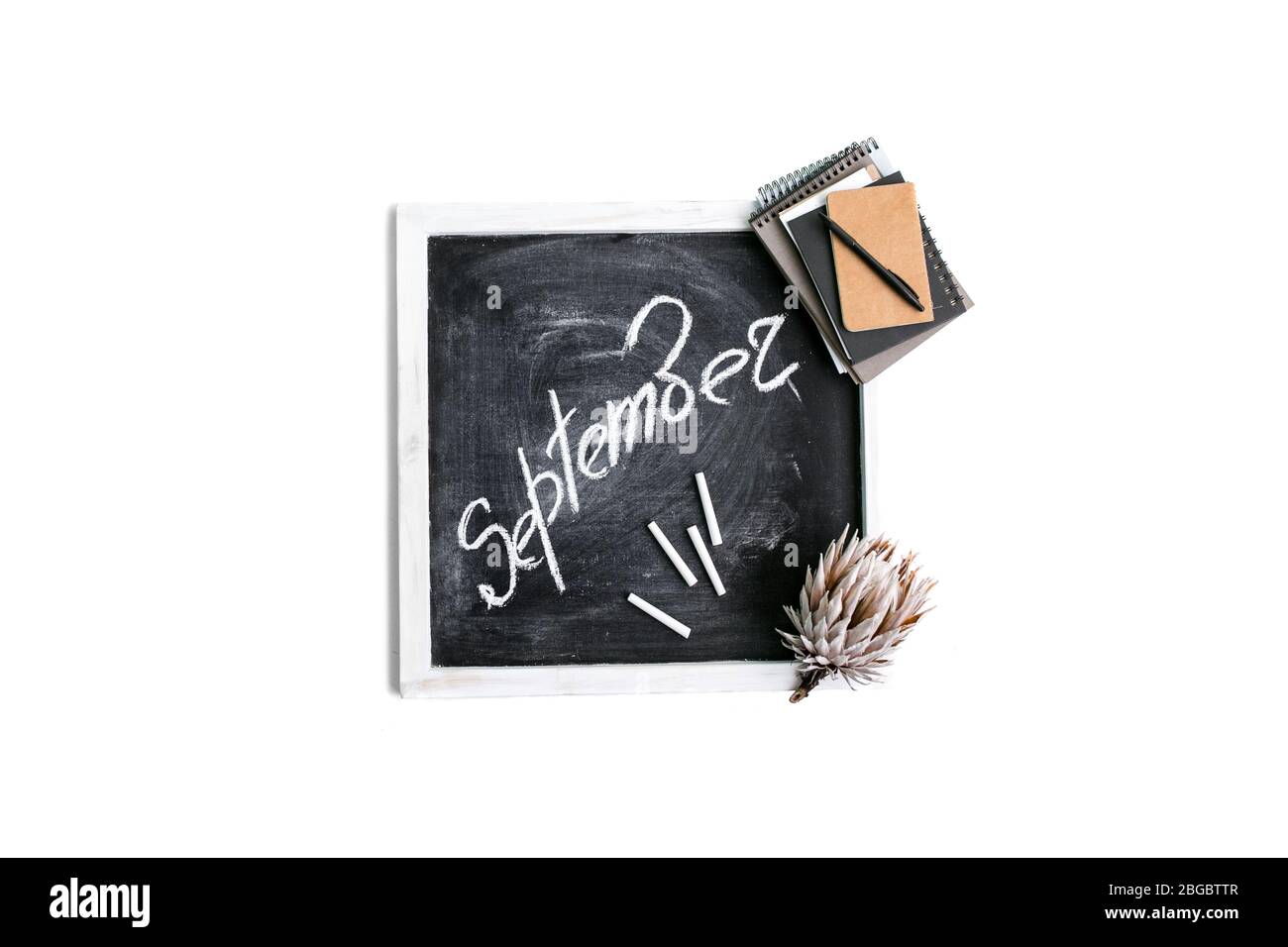 The inscription 'SEPTEMBER' is chalked with notebooks and flower on a black wooden background. Flat lay, top view Stock Photo
