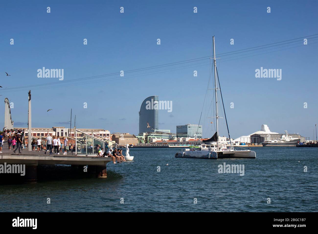 View of catamaran and people hanging out at Barcelona port. It is a sunny summer day. Stock Photo