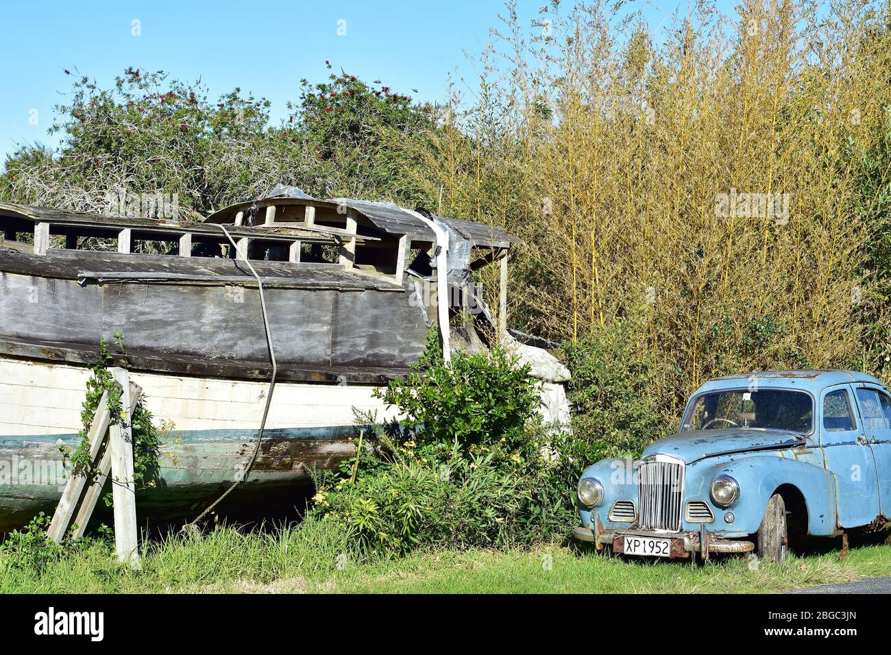 Rusty vintage car with registration plate next to rotting wooden motor