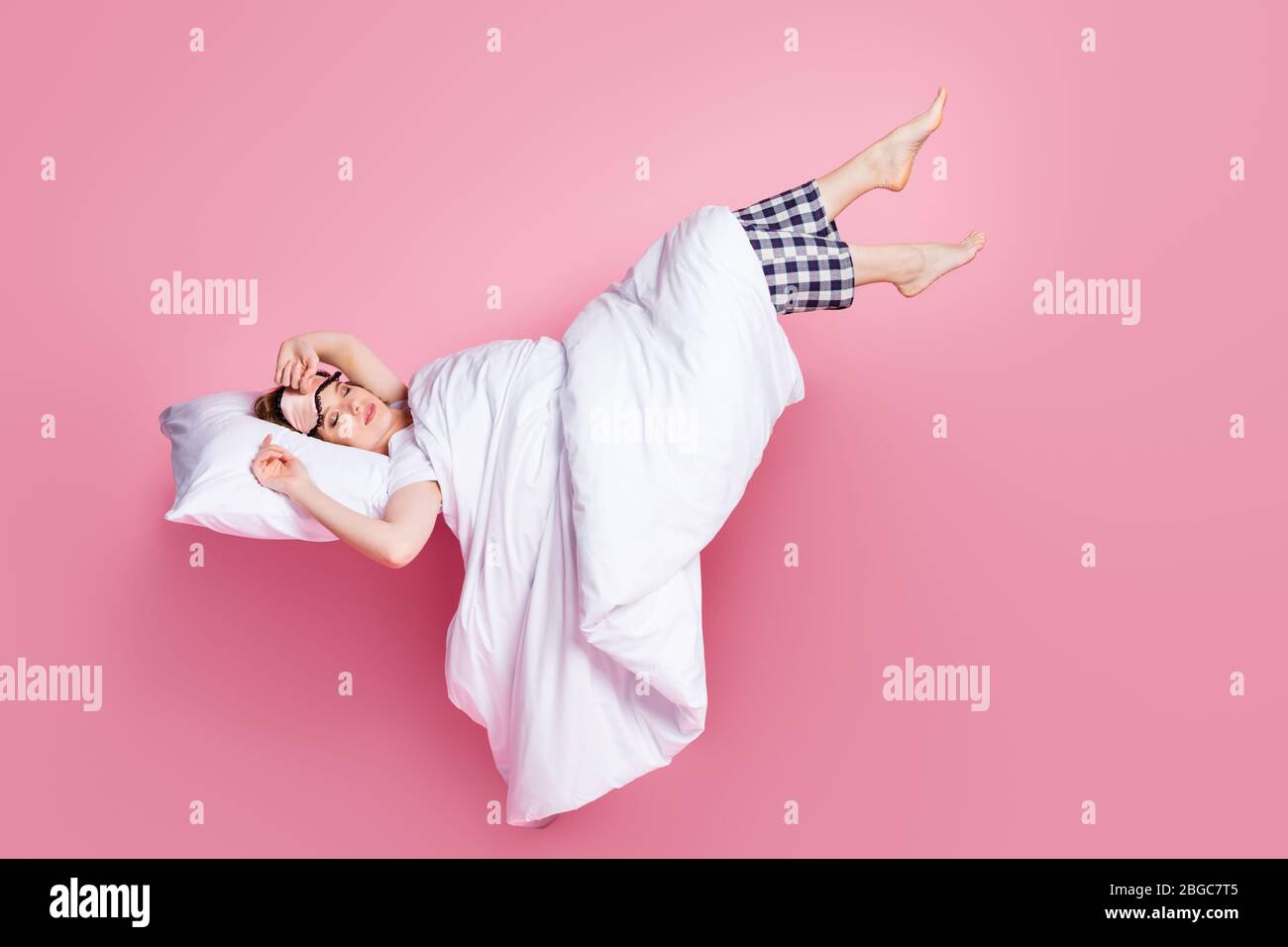 Full size photo of pretty lady saturday nap lying bed pillow blanket sleep and walk raise legs empty space wear mask white t-shirt pajama pants Stock Photo