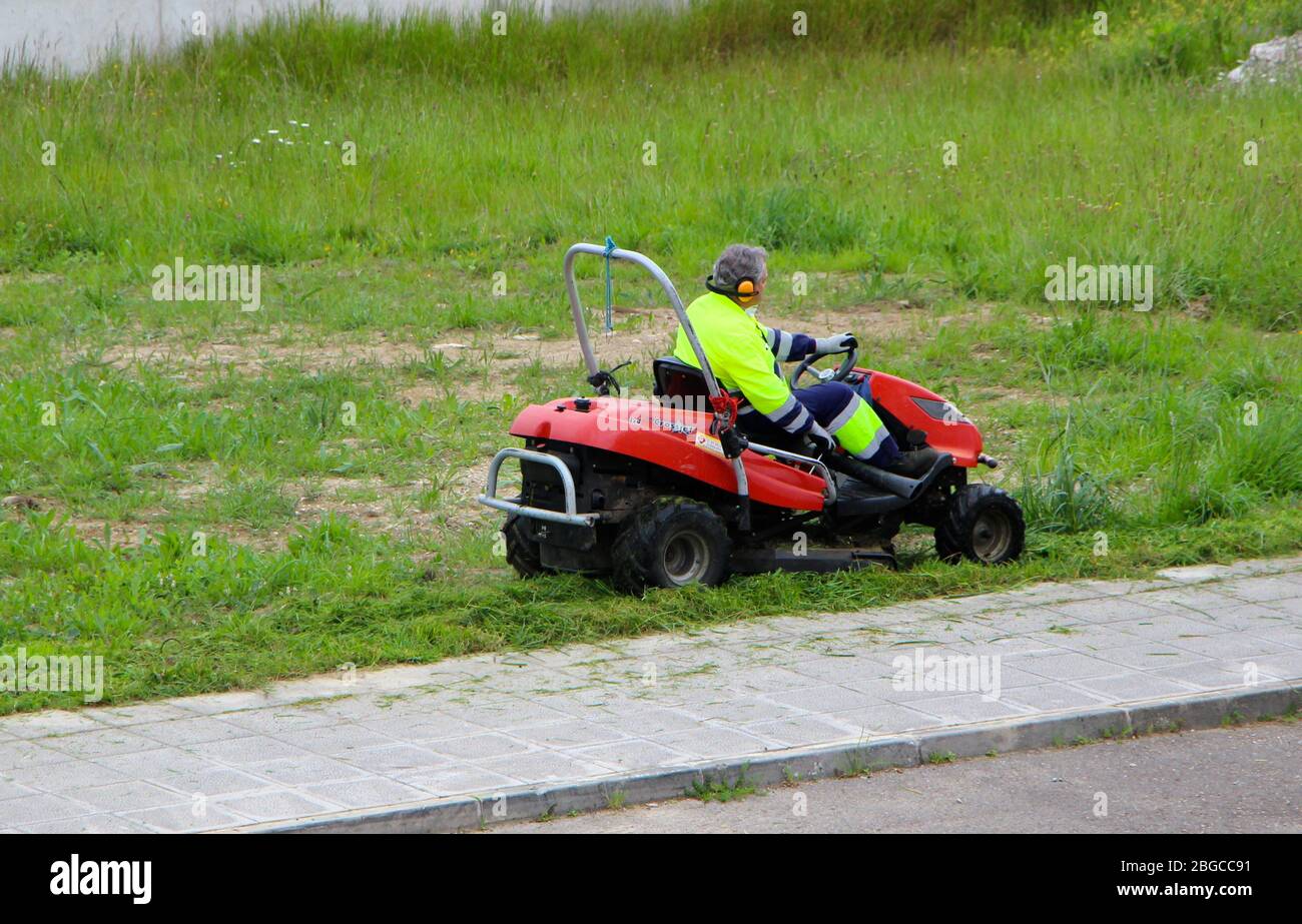 Ride on lawn mower being driven along the edge of the pavement by a