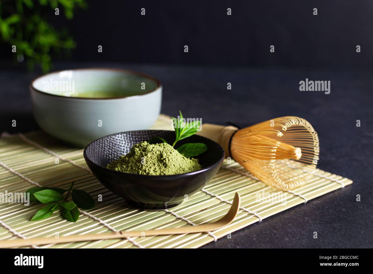 Organic green matcha tea and tea accessories on japanese mat on black background. Japanese tea ceremony concept. Chashaku spoon and chasen bamboo whis Stock Photo