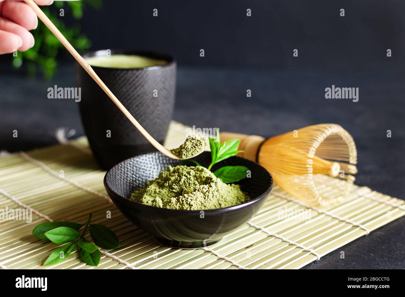 Organic green matcha tea and tea accessories on japanese mat on black background. Japanese tea ceremony concept. Chashaku spoon and chasen bamboo whis Stock Photo