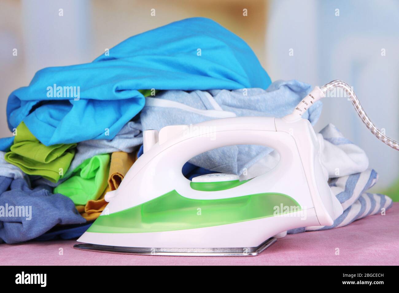 iron-and-pile-of-colorful-clothes-on-table-on-bright-background-stock