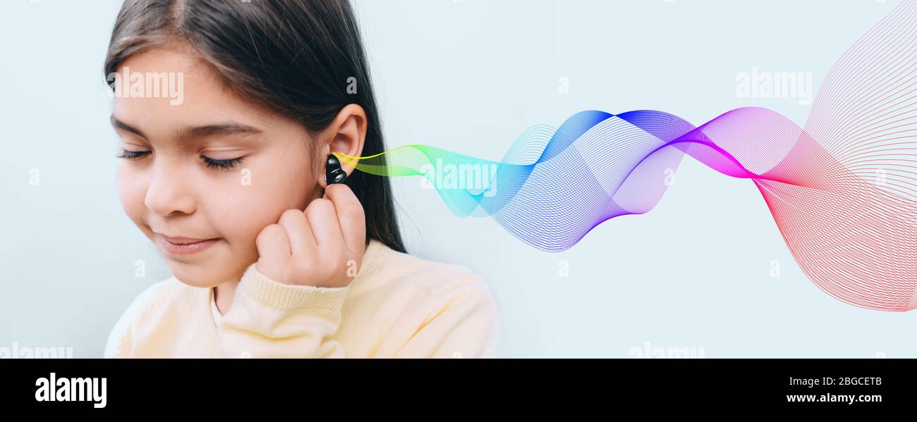 Cute mixed race child holding hearing aid near her ear. Colored sound waves showing variety of sounds going to the ear. It's great to hear Stock Photo