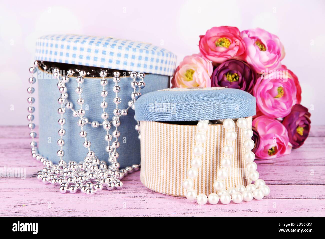 Decorative boxes with beads and flowers on table on bright background Stock Photo