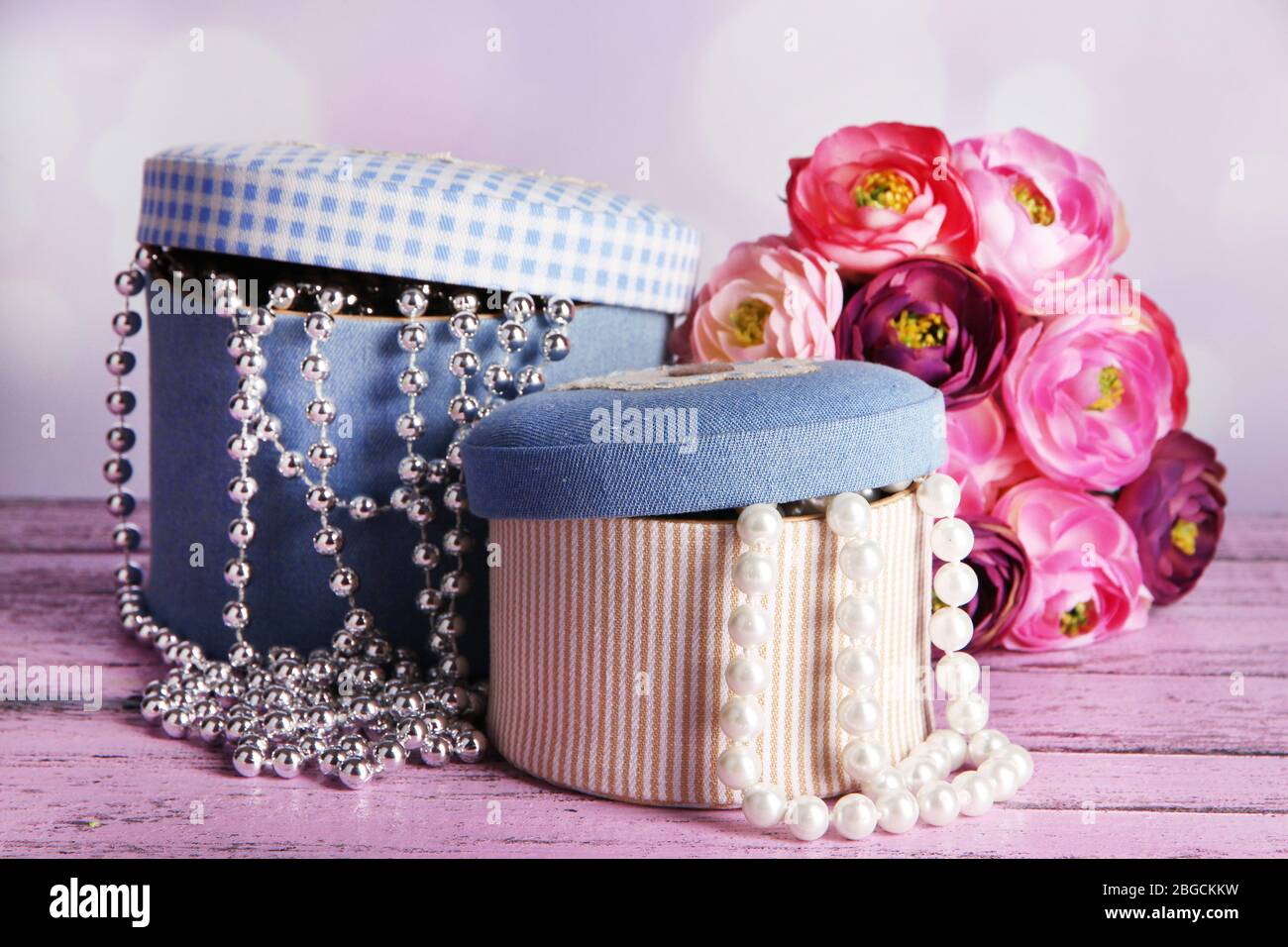 Decorative boxes with beads and flowers on table on bright background Stock Photo