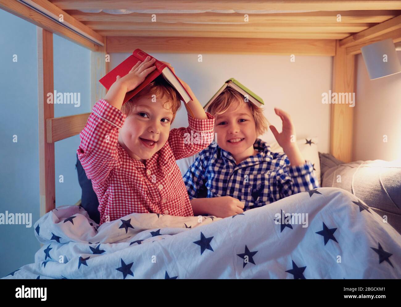 cheerful kids, brothers having fun, playing with books on the bunk bed during bedtime Stock Photo