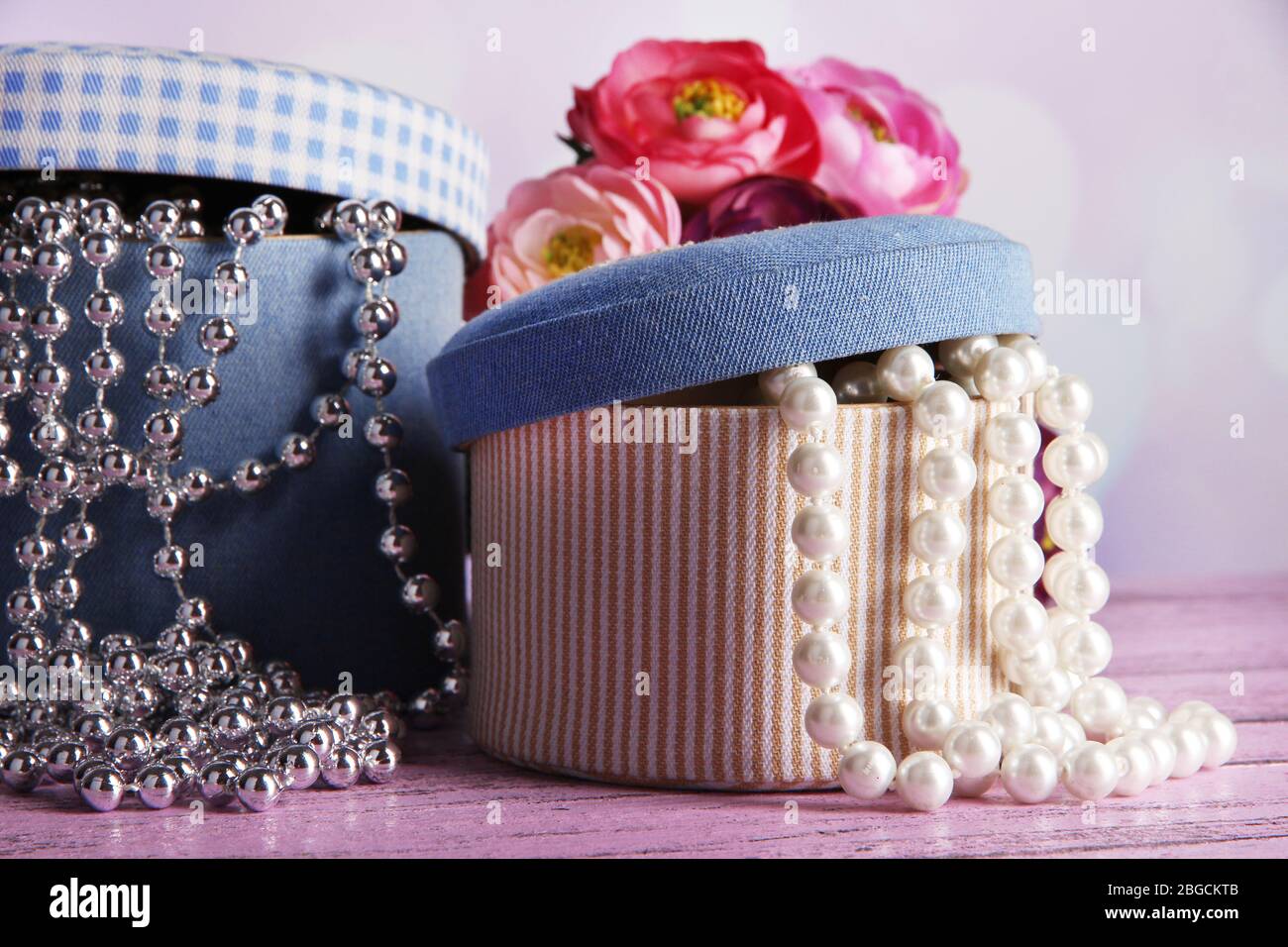 Decorative boxes with beads and flowers on table on bright background Stock Photo