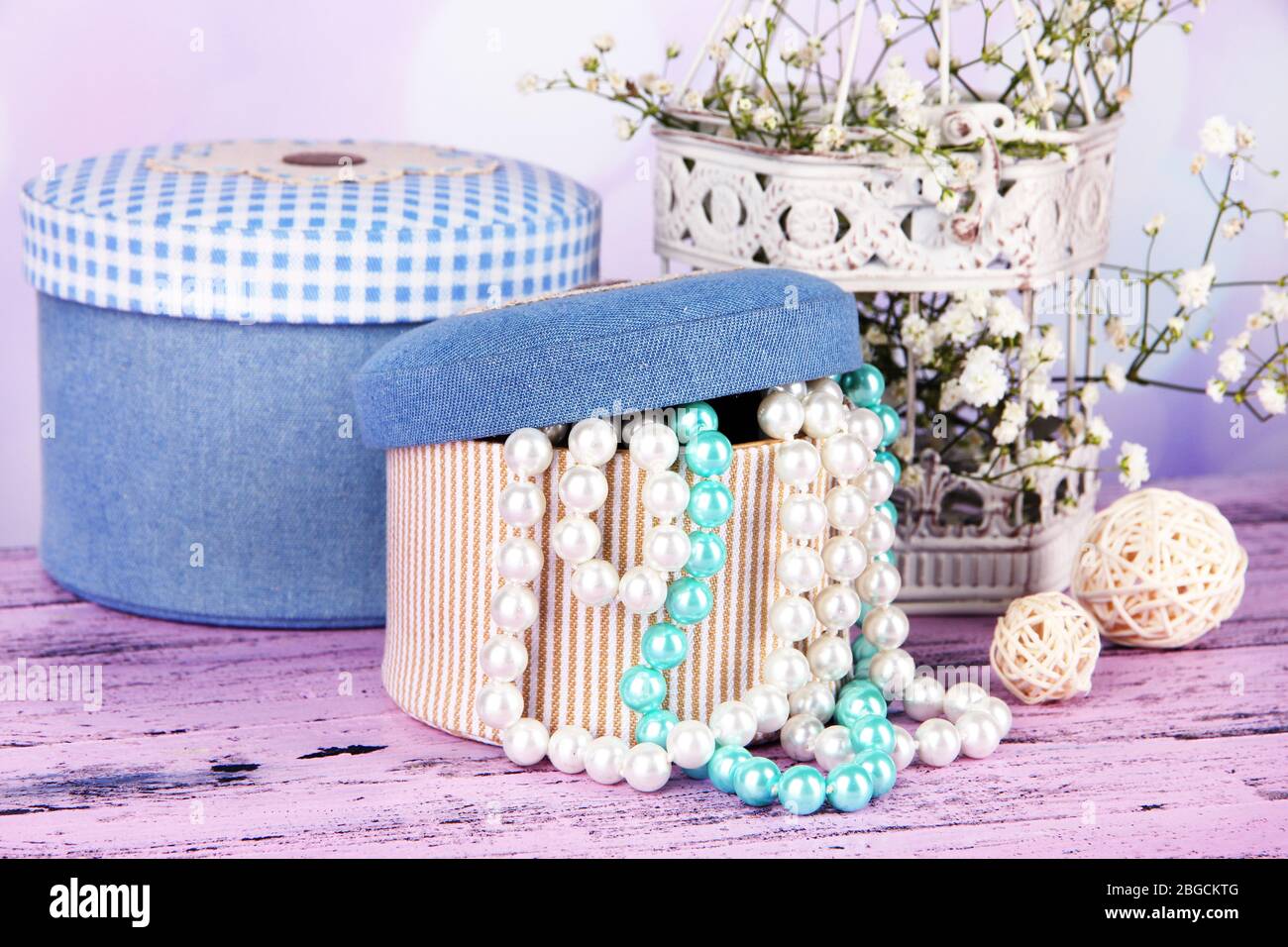 Decorative boxes with beads and flowers on table on bright background Stock Photo