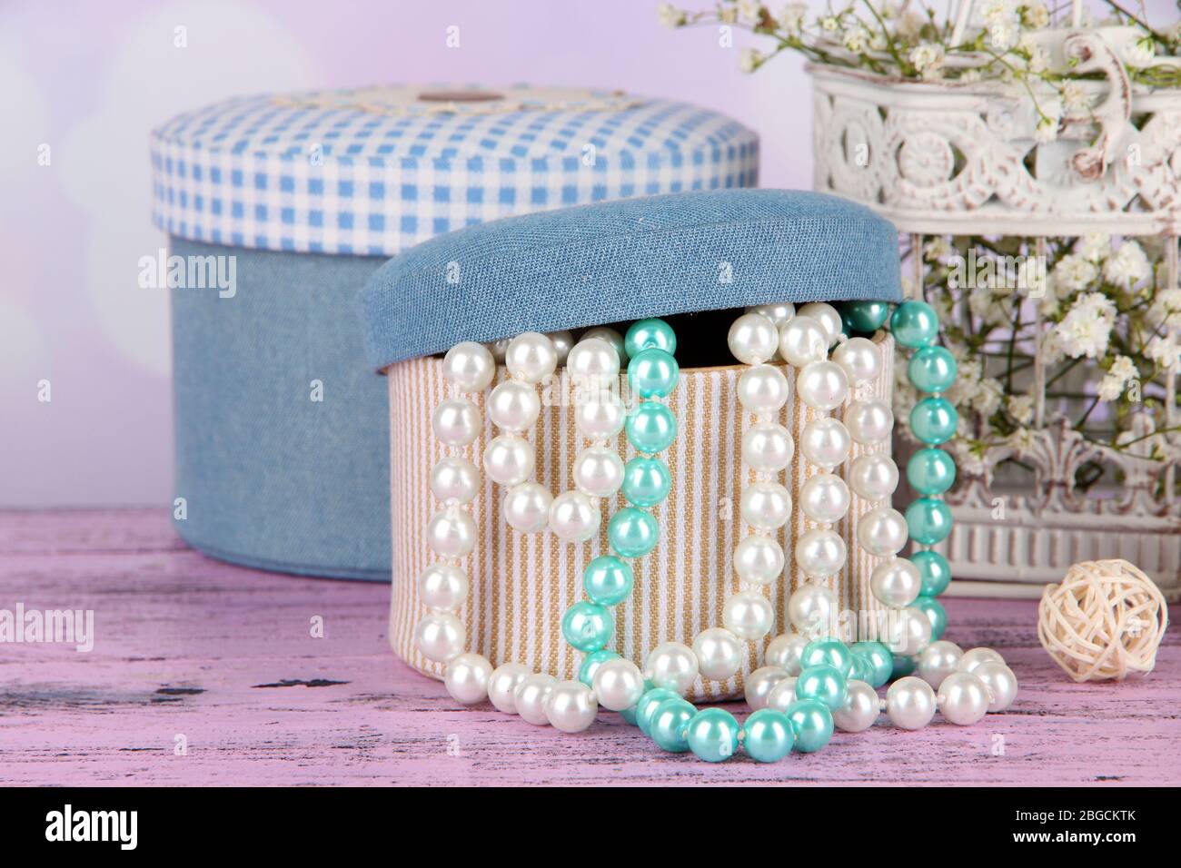Decorative boxes with beads and flowers on table on bright background Stock Photo