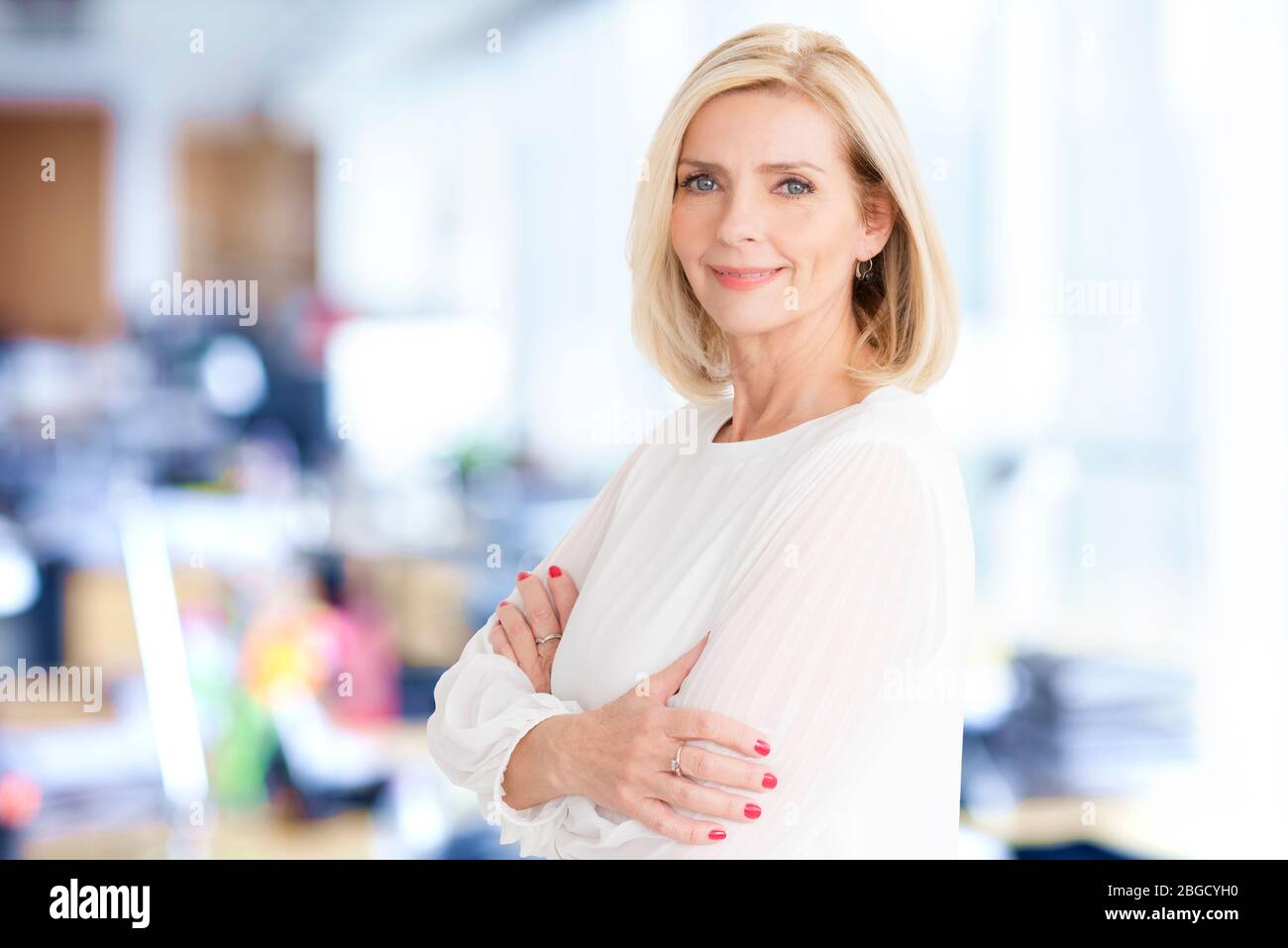 Close-up portrait of beautiful blond businesswoman standing in the office while looking at camera and smiling. Stock Photo