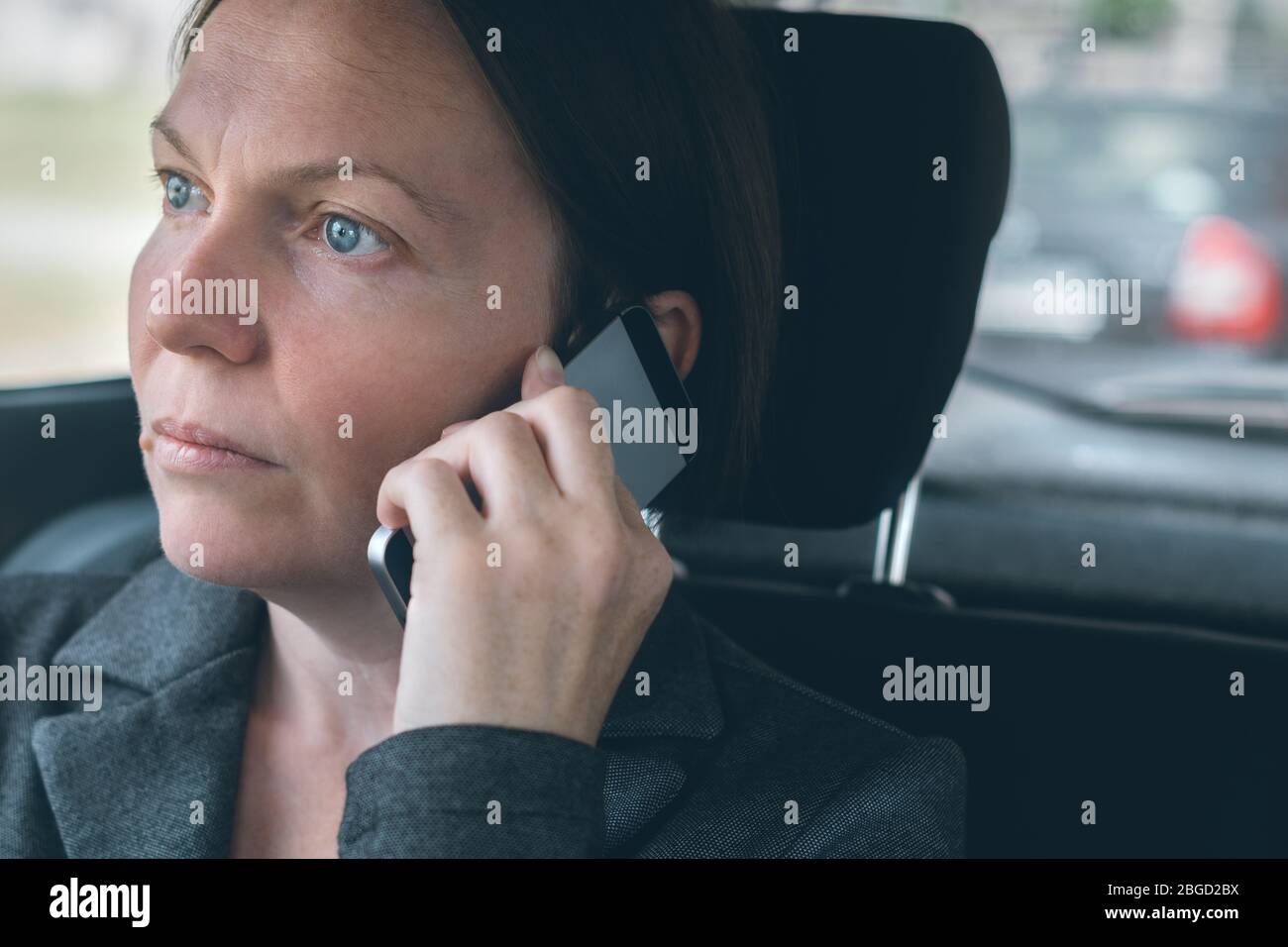 Businesswoman talking on mobile phone on car back seat, business on the move concept. Elegant adult caucasian female person using smartphone for commu Stock Photo