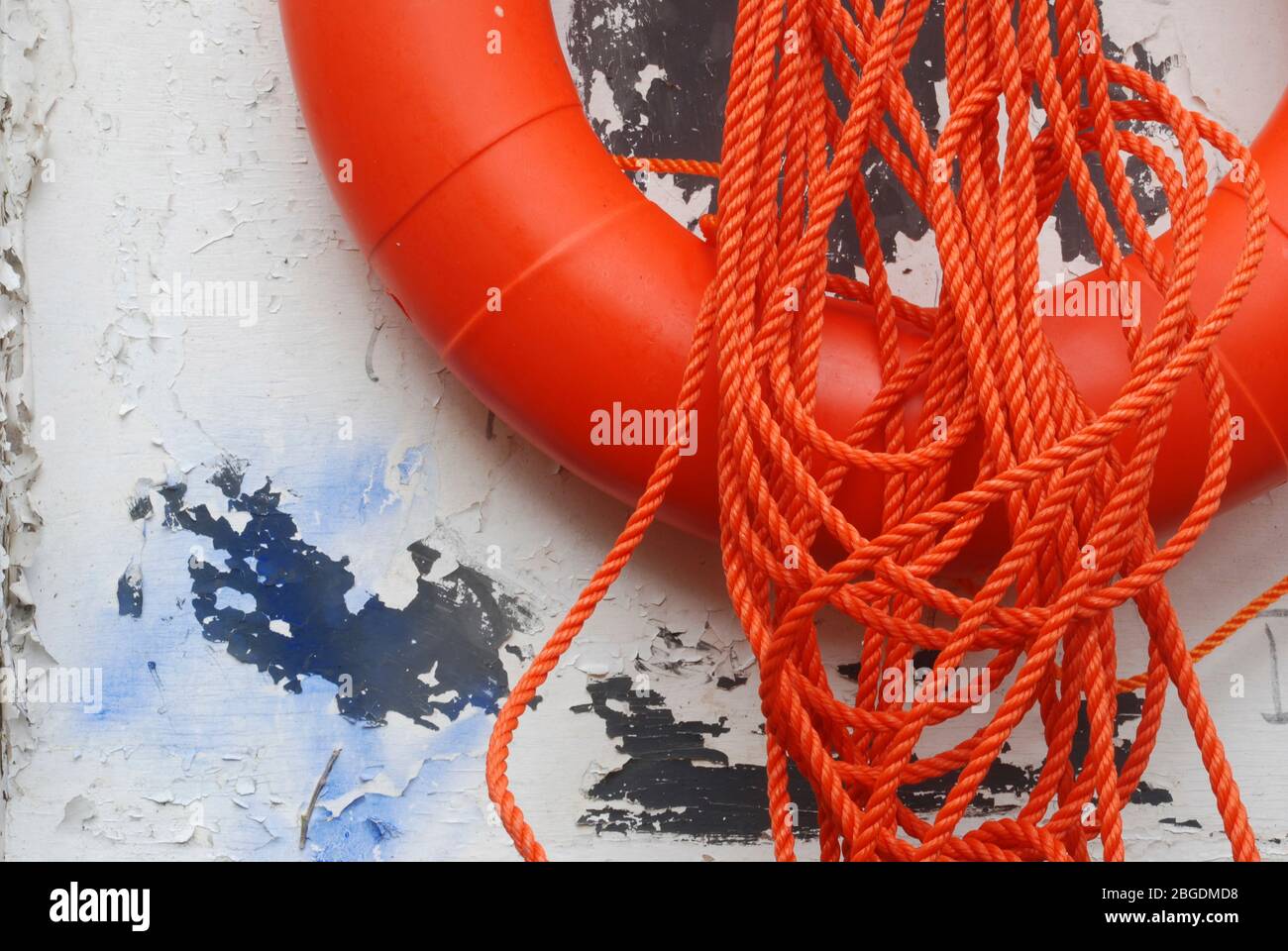 Close image of lower half of bright orange life belt with orange cord looped and attached to wooden board which has flaking white paint Stock Photo