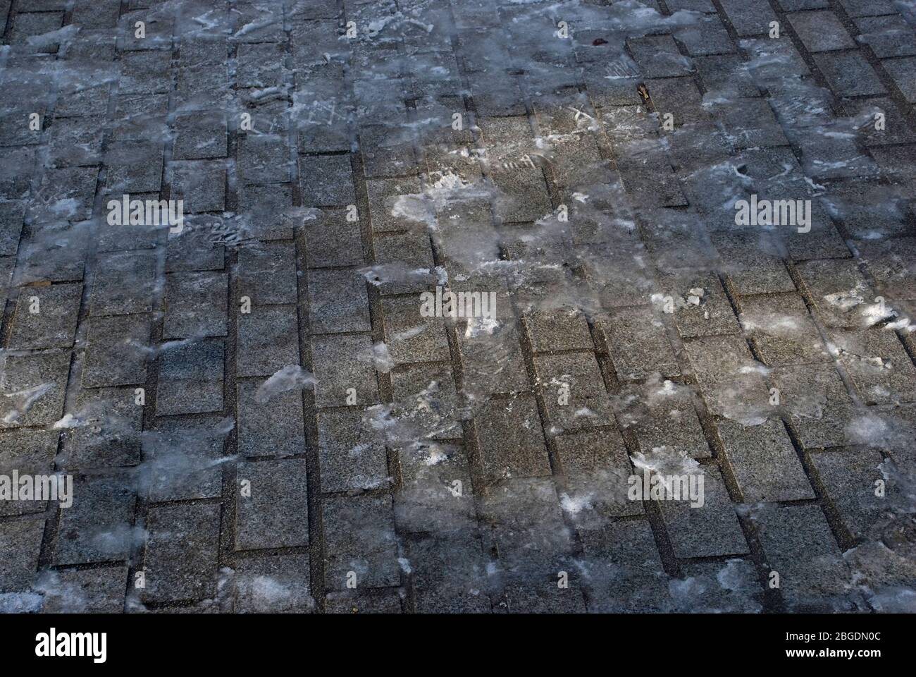 Street block paving in winter with a thin layer of ice and footprints and a small pool of light Stock Photo