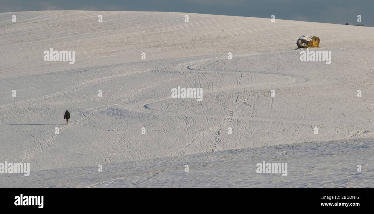 Snowy landscape scene with a distant lone figure trudging through the snow towards a large stone memorial with a curving path also visible Stock Photo
