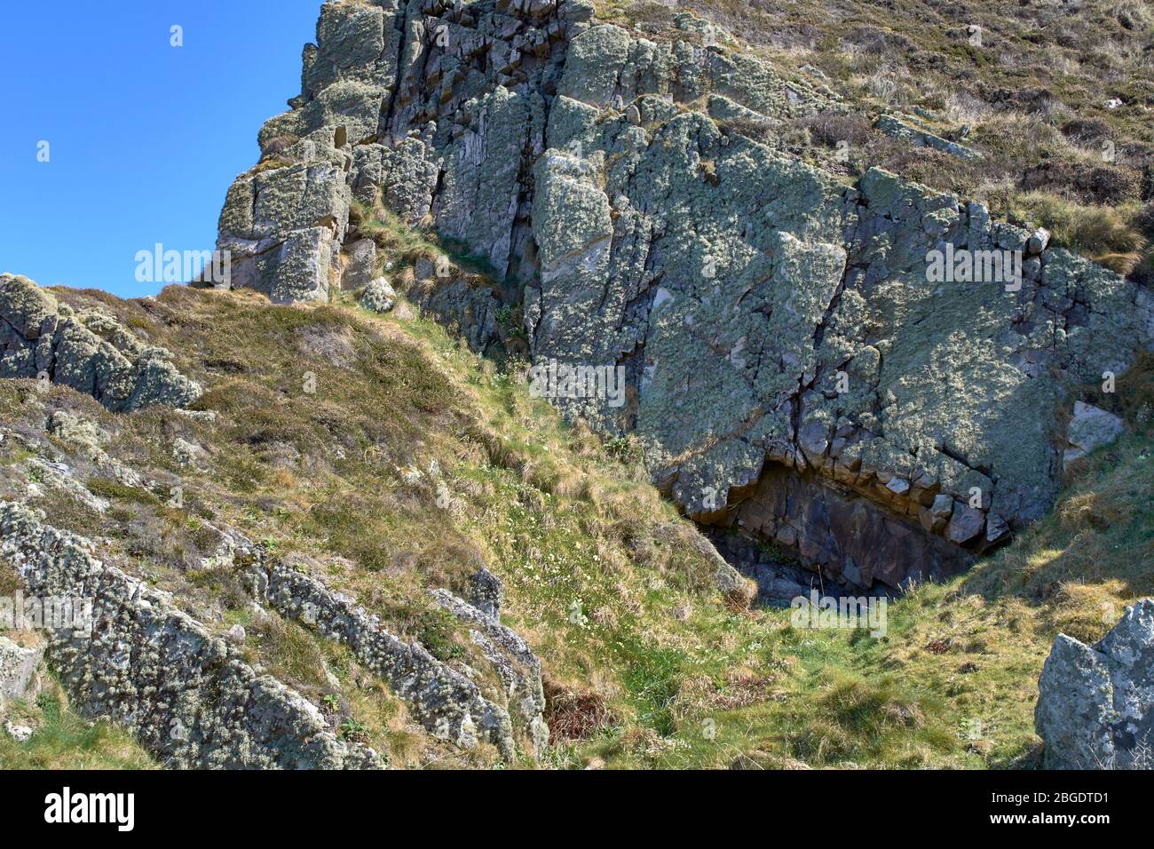 SUNNYSIDE BAY CULLEN MORAY FIRTH SCOTLAND EN ROUTE TO THE BEACH A SMALL CAVE SURROUNDED BY GREEN LICHEN COVERED ROCKS Stock Photo