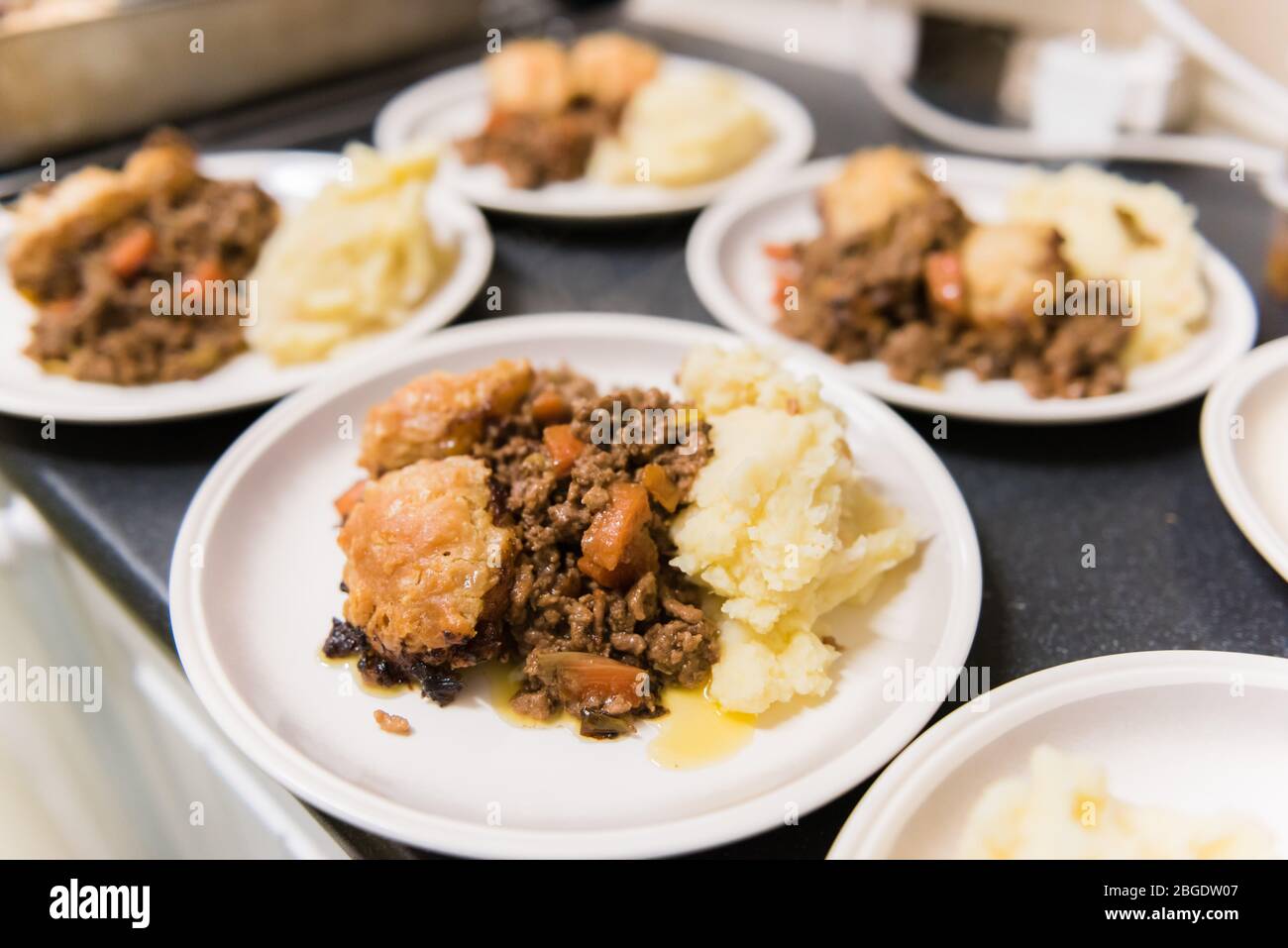 A traditional British school dinner classic, Beef Stew, dumplings and mash, being served up at a community food organisation in a village hall Stock Photo