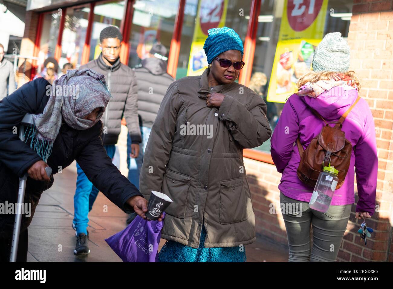 A woman walks past a beggar holding out a donation cup on Brixton Road, London Stock Photo