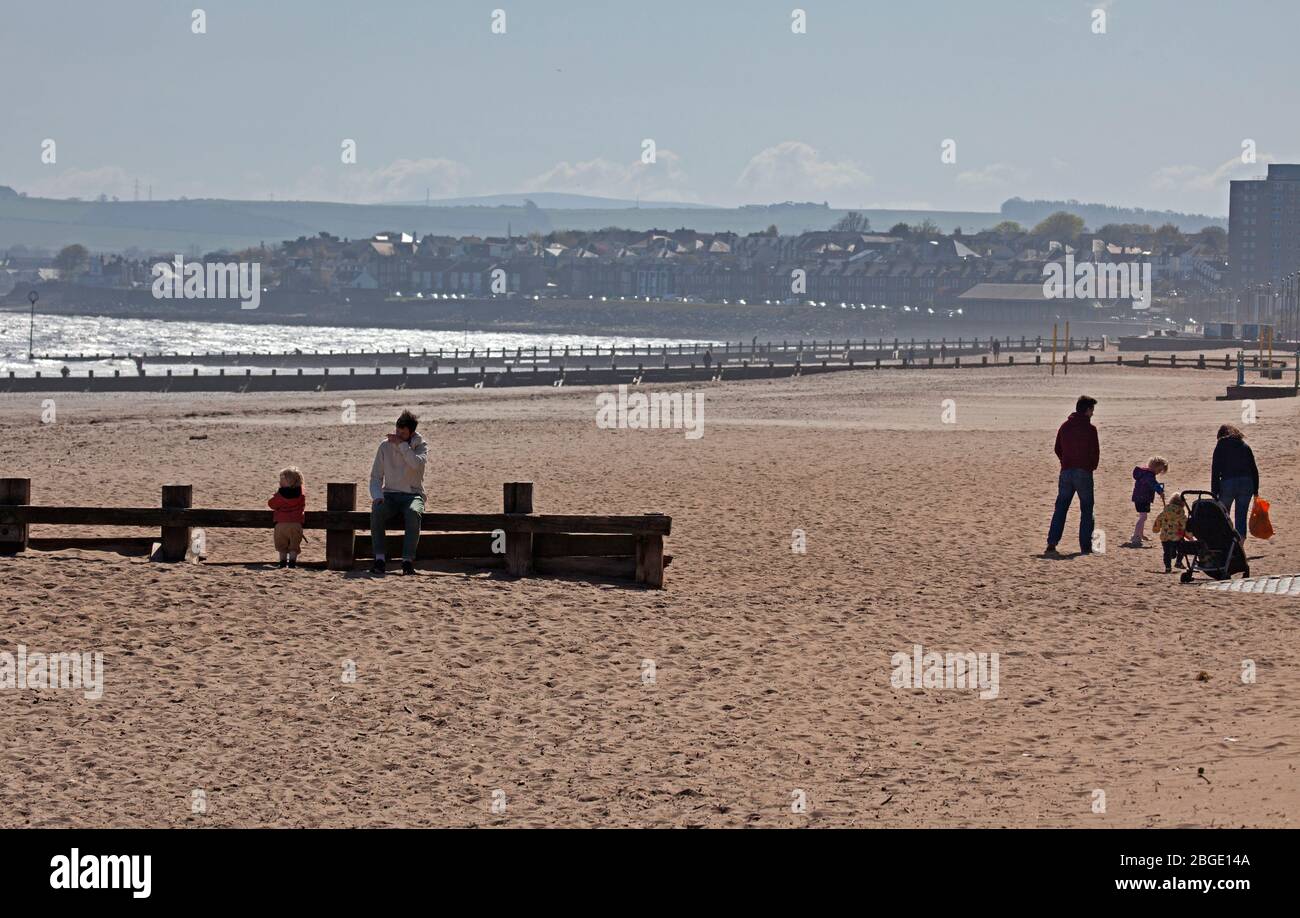 Portobello, Edinburgh, Scotland, UK. 21st April 2020. As Coronavirus Lockdown continues the public who are out before noon enjoy the sunshine at the seaside however, a cool ENE wind of 30km/h with potential gusts of 46 km/h does not encourage those that are out to sit for very long. Three places are now opening for take away food, Muro's Bistro, The  Beach House and the Espy Pub has removed the shutters from their windows. Credit: Arch White/ Alamy Live News. Stock Photo